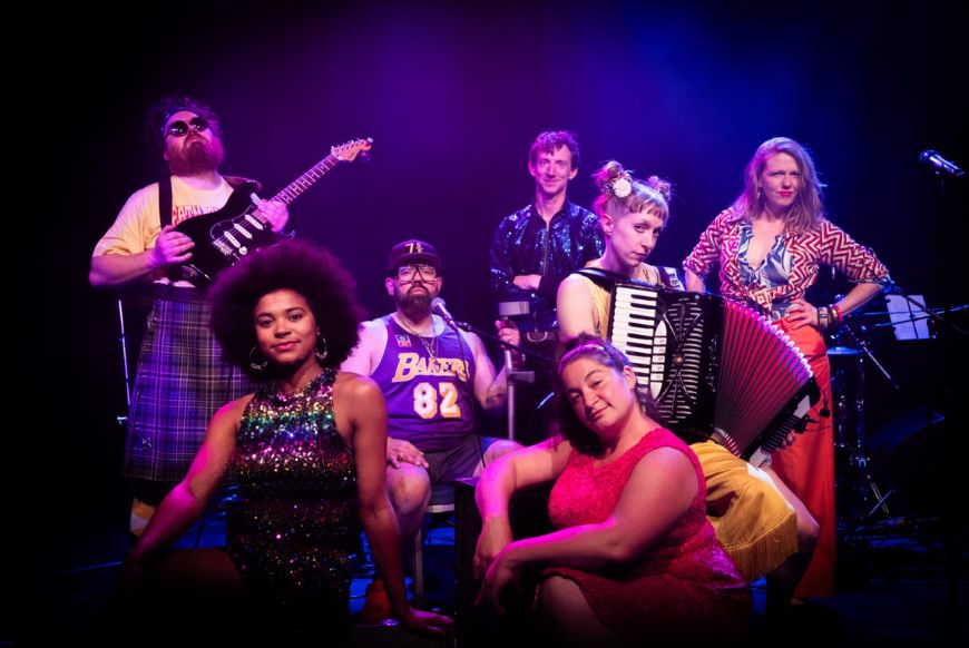 7 people on a stage, each holding different instruments